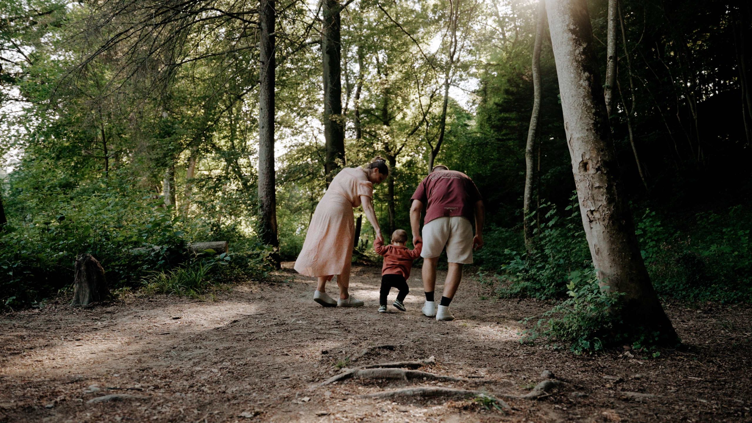 Eine Familie mit einem Kleinkind läuft gemeinsam in einem Waldstück